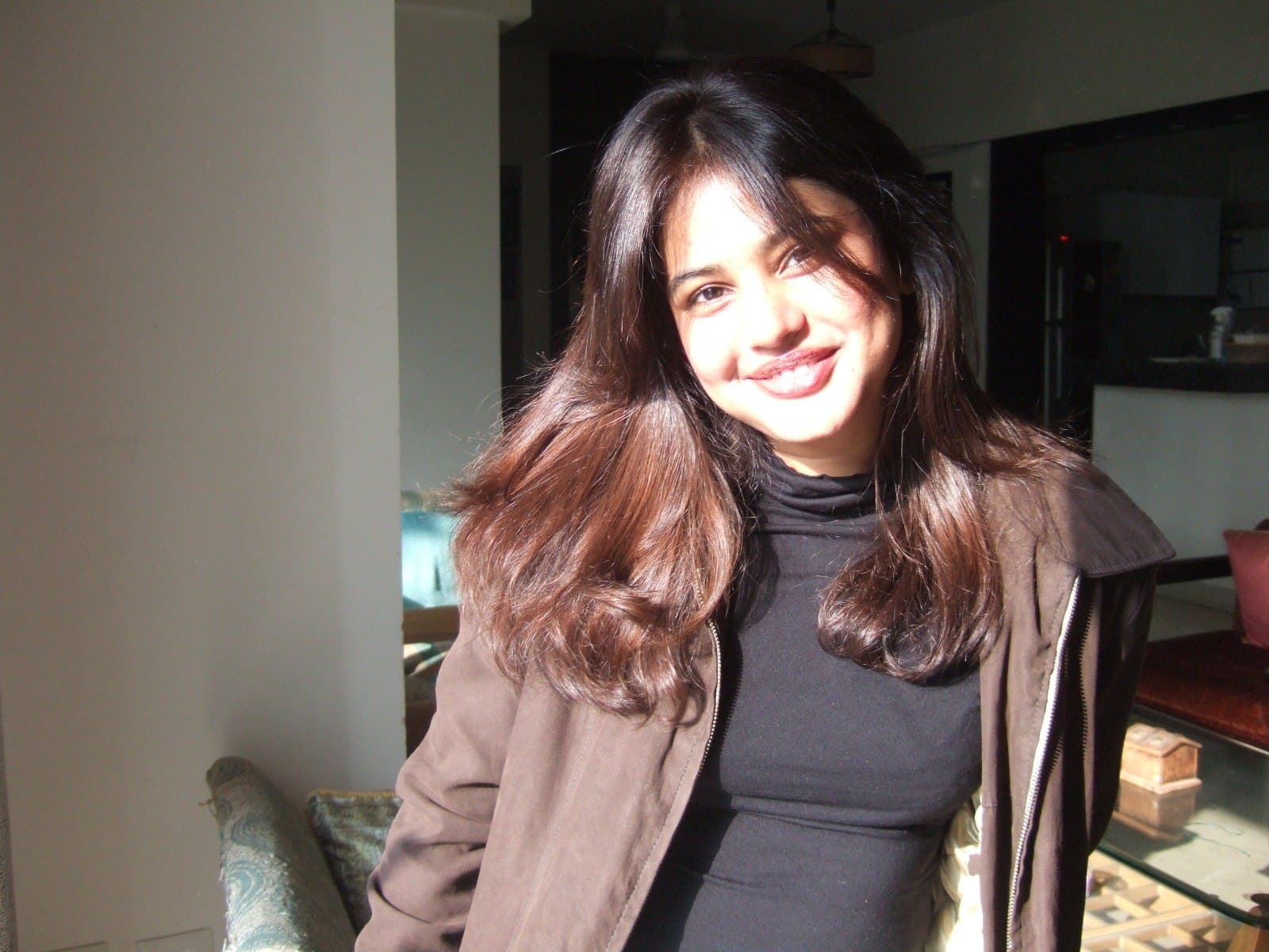 Swapnaja smiling in low winter sunlight, in a brown jacket over a black turtleneck.